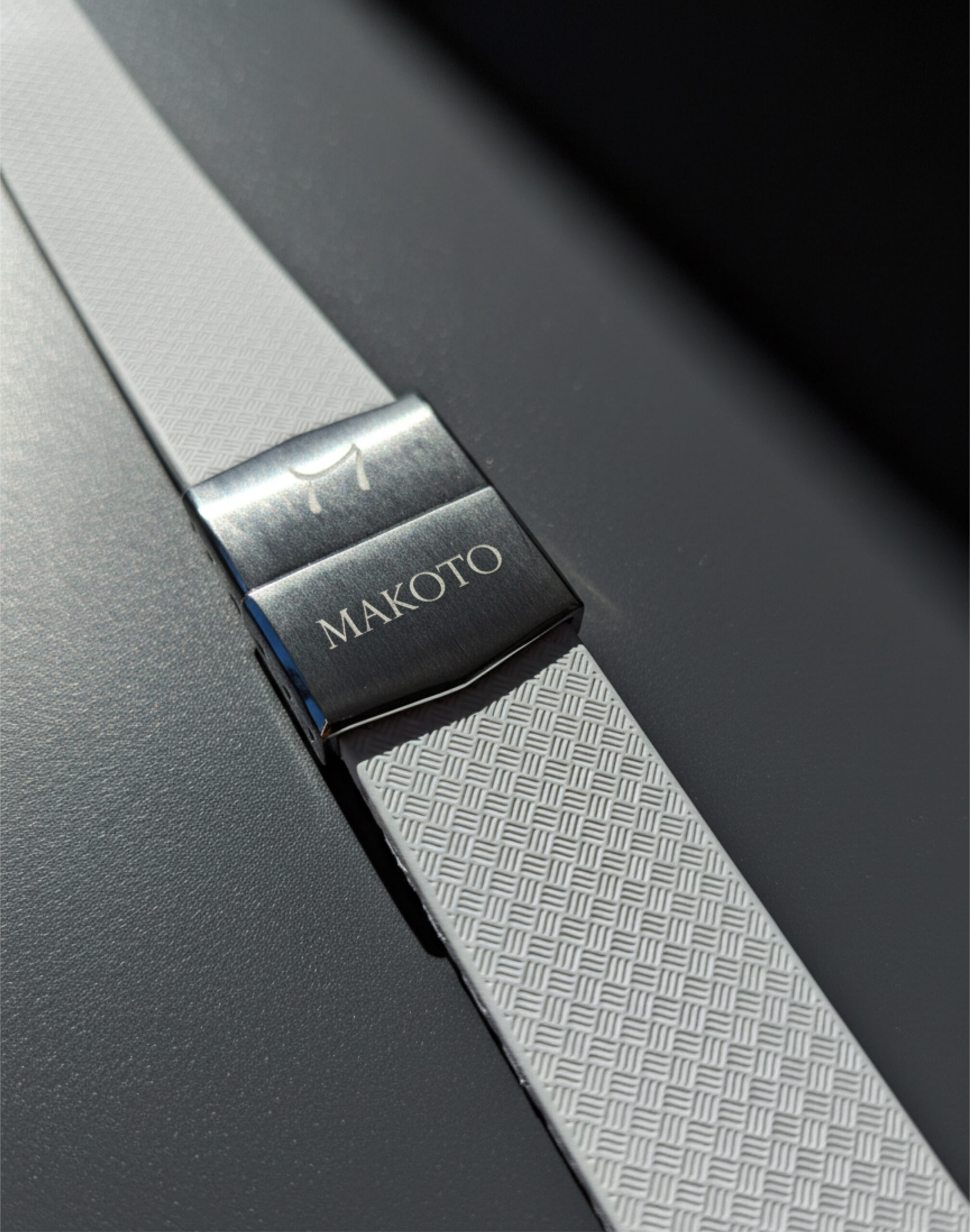 Close-up of a white textured strap with a metallic clasp engraved 'MAKOTO'.