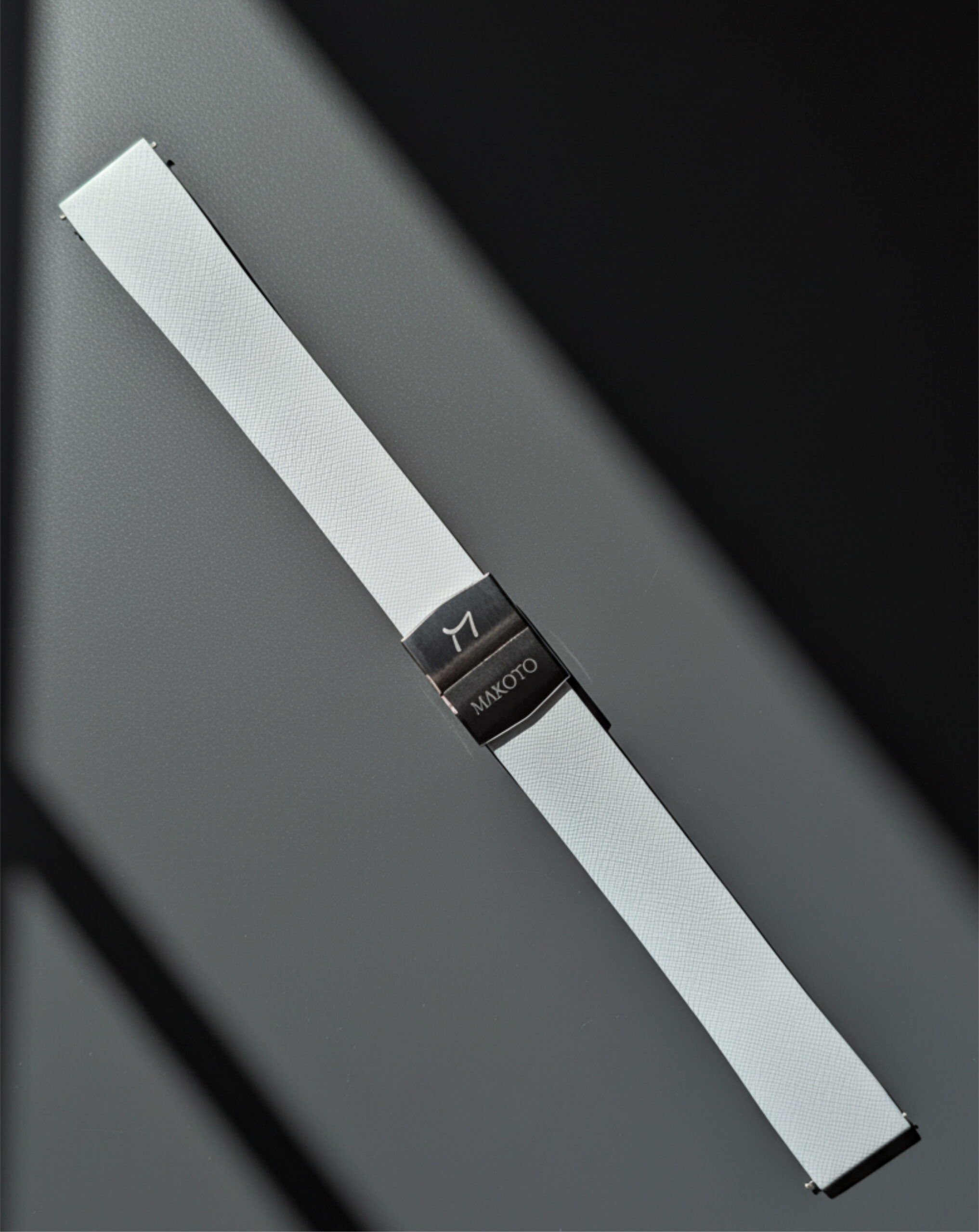 Close-up of a white smartwatch band with a black buckle on a gray background.