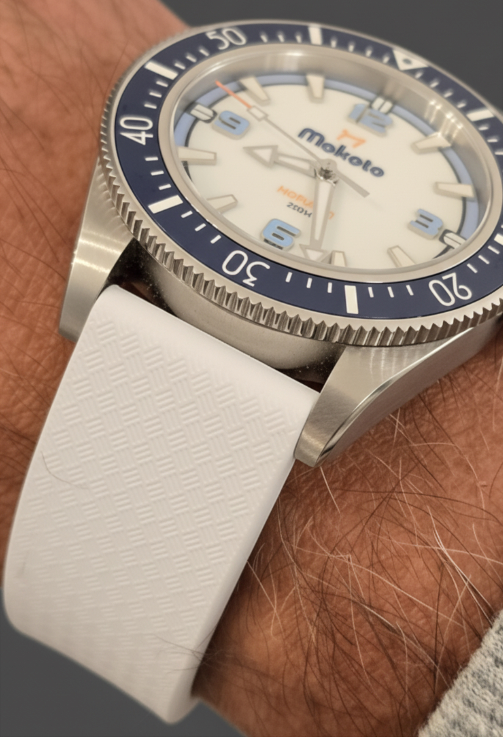 Close-up of a wristwatch with a white strap and blue bezel on a wrist.