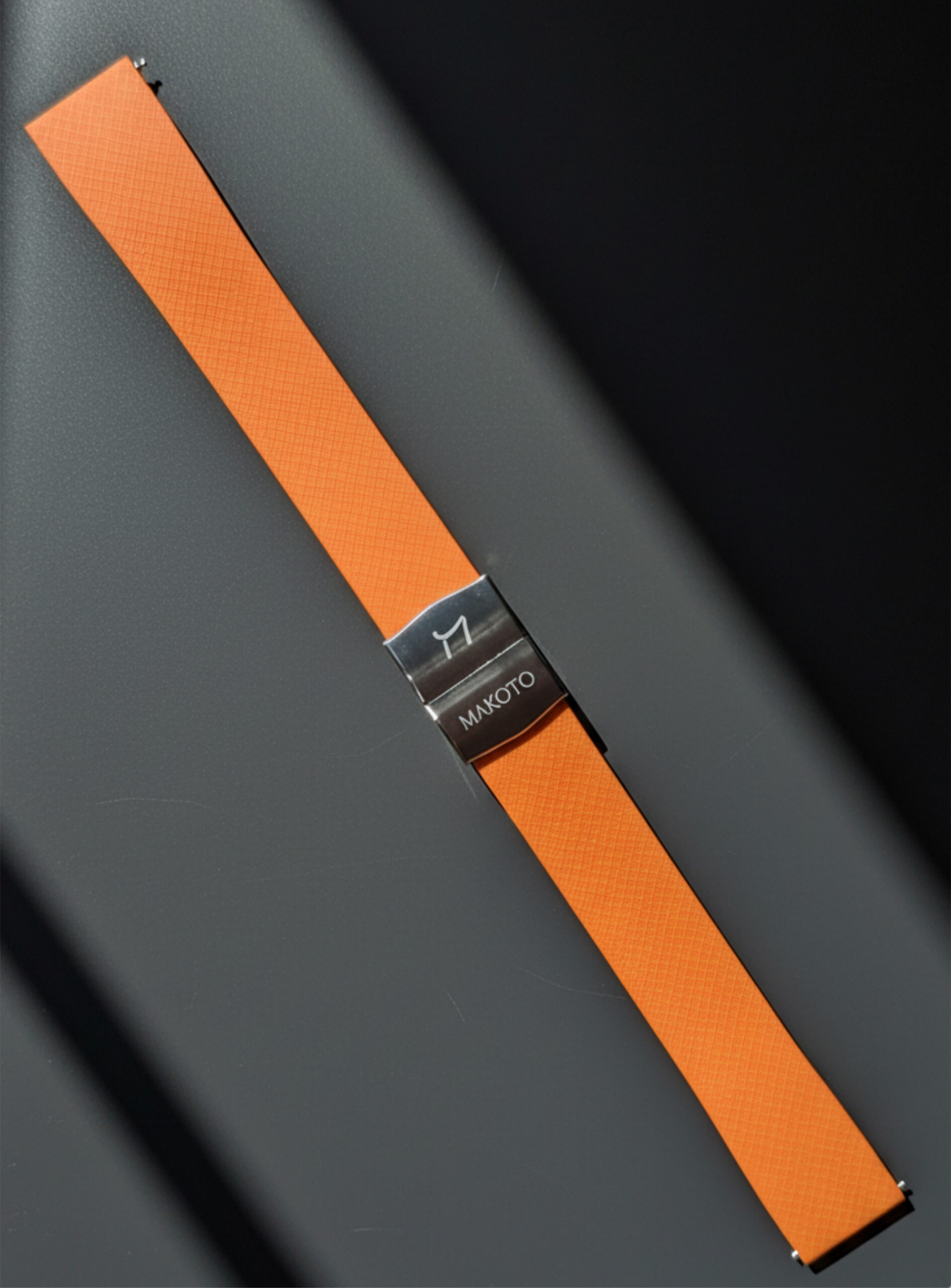 Close-up of an orange watch strap with a metal clasp on a dark surface.
